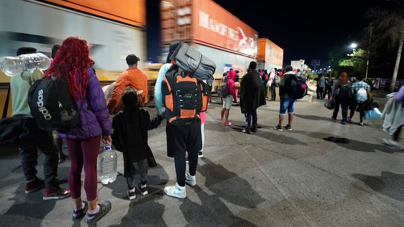 Migrantes miran un tren de mercancías mientras esperan a un tren rumbo al norte que se detenga...
